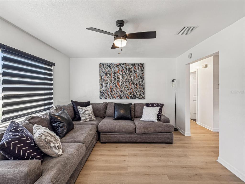A living room features a gray sectional sofa, abstract wall art, and light wood flooring — 2000 57TH STREET N, ST PETERSBURG, FL