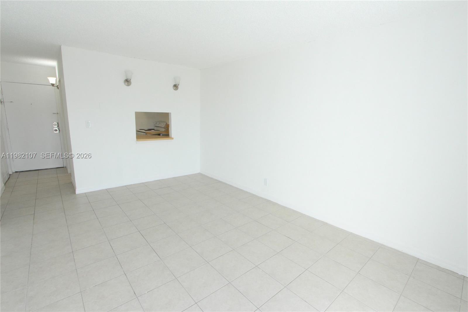 An empty room features white walls, light-colored tile flooring, and a small kitchen pass-through window — 4550 NW 9th St # 815E, Miami FL 33126, MIAMI, FL