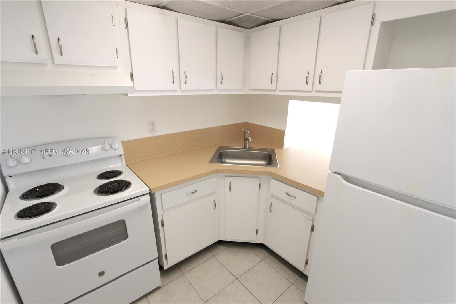 A small kitchen features white cabinets, a corner sink, and white appliances — 4550 NW 9th St # 815E, Miami FL 33126, MIAMI, FL