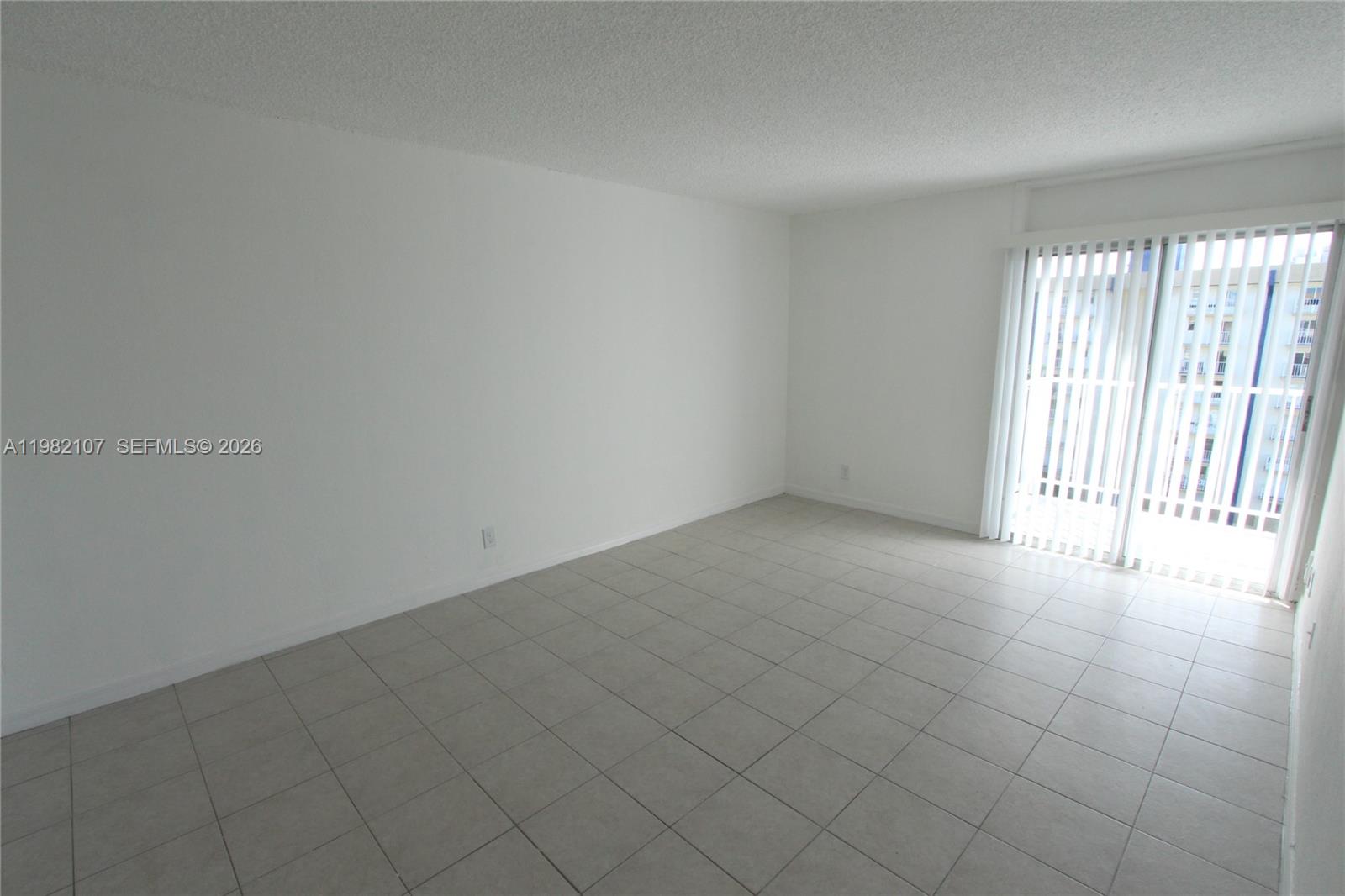 An empty room features white walls, light-colored tile flooring, and a sliding glass door — 4550 NW 9th St # 815E, Miami FL 33126, MIAMI, FL