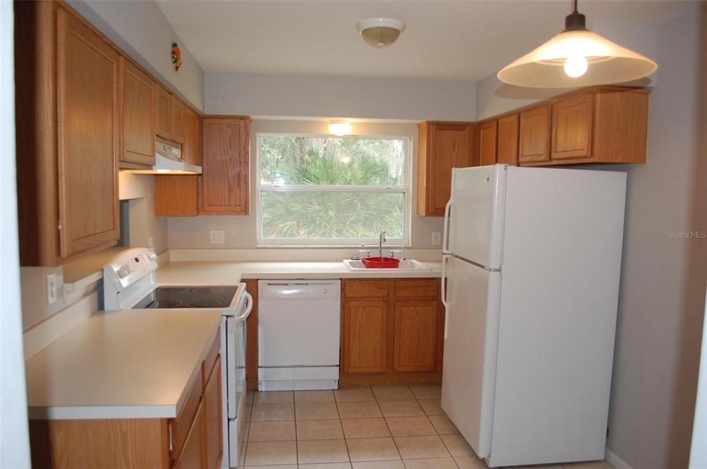 A kitchen with oak cabinets, white appliances, tile flooring, and a window above the sink — 2887 N BERMUDA AVENUE, APOPKA, FL