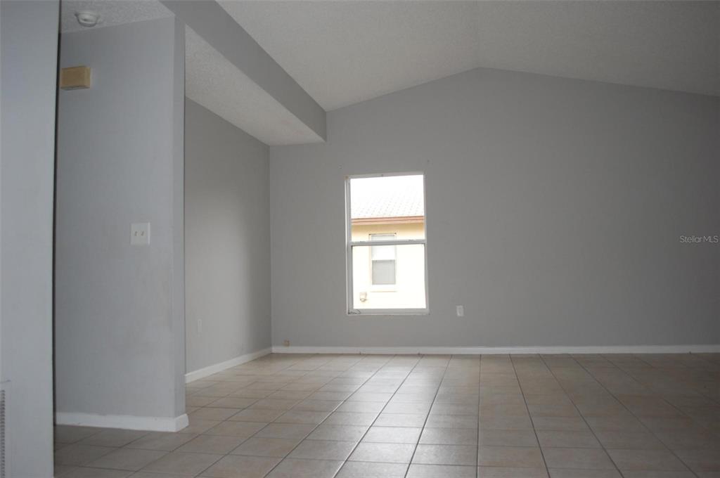 An empty room features light gray walls, a vaulted ceiling, and beige tiled flooring — 2887 N BERMUDA AVENUE, APOPKA, FL