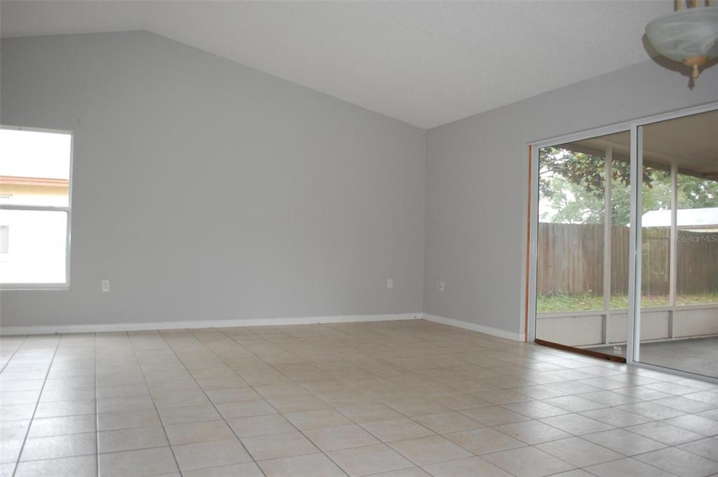 An empty room with light gray walls, tile flooring, a vaulted ceiling, and sliding glass doors — 2887 N BERMUDA AVENUE, APOPKA, FL