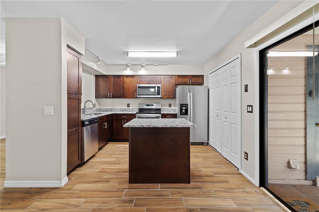 A kitchen with dark wood cabinets, granite countertops, stainless steel appliances, and wood-look tile flooring — 2941 LOWELL COURT, CASSELBERRY, FL