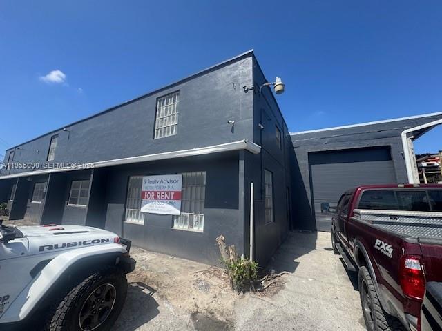 A dark gray industrial building with a for rent sign sits between a Jeep and truck — 7130 NW 35th Ave, Miami FL 33147, MIAMI, FL