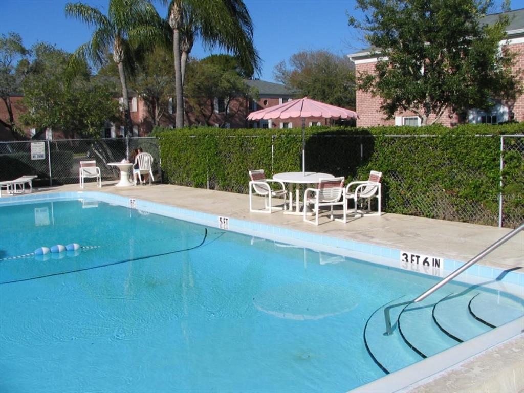 A swimming pool with a patio area, outdoor furniture, and a pink umbrella — 1143 85TH TERRACE N UNIT D, ST PETERSBURG, FL