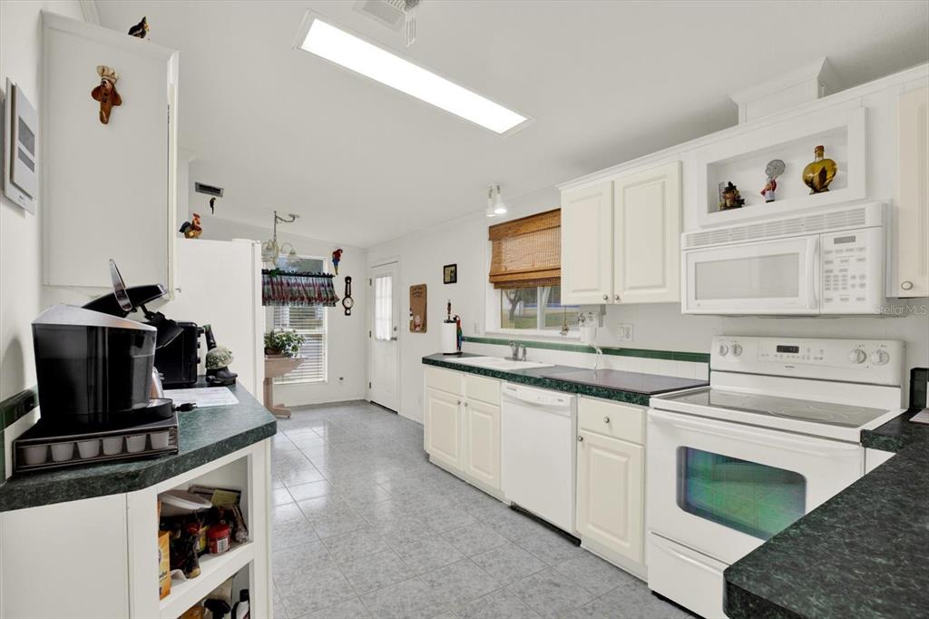 A kitchen features white cabinets, green countertops, tile flooring, and a white appliance suite — 8010 CEDAR COVE AVENUE, BROOKSVILLE, FL
