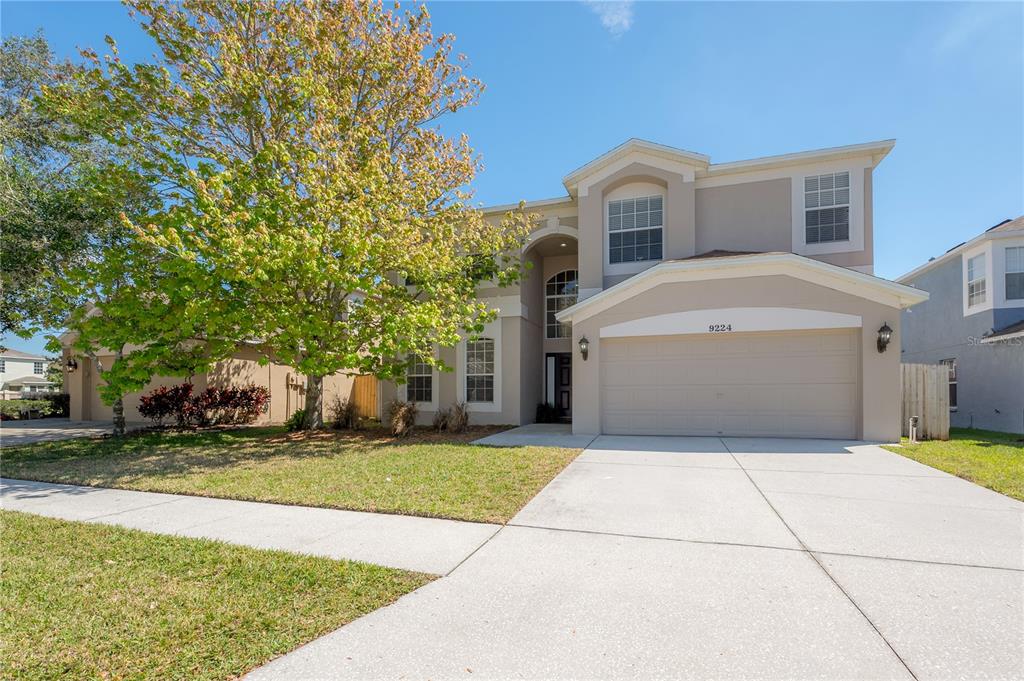 A two-story suburban house features a beige stucco exterior, a two-car garage, and a tree — 9224 LOST MILL DRIVE, LAND O LAKES, FL