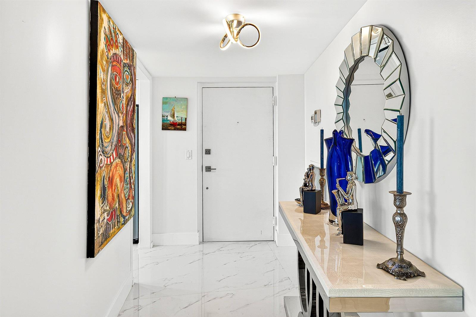A bright entryway features white walls, marble-look tile flooring, a console table, and wall art — 3360 S Ocean Boulevard, Palm Beach FL 33480, PALM BEACH, FL