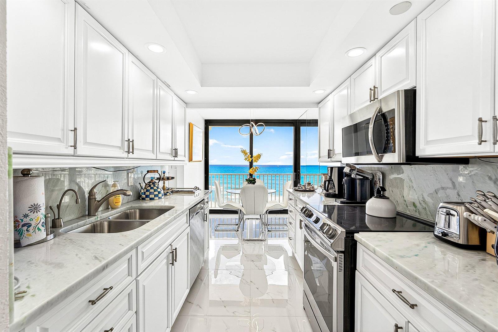 A galley kitchen with white cabinets, marble countertops, and a view of the ocean — 3360 S Ocean Boulevard, Palm Beach FL 33480, PALM BEACH, FL