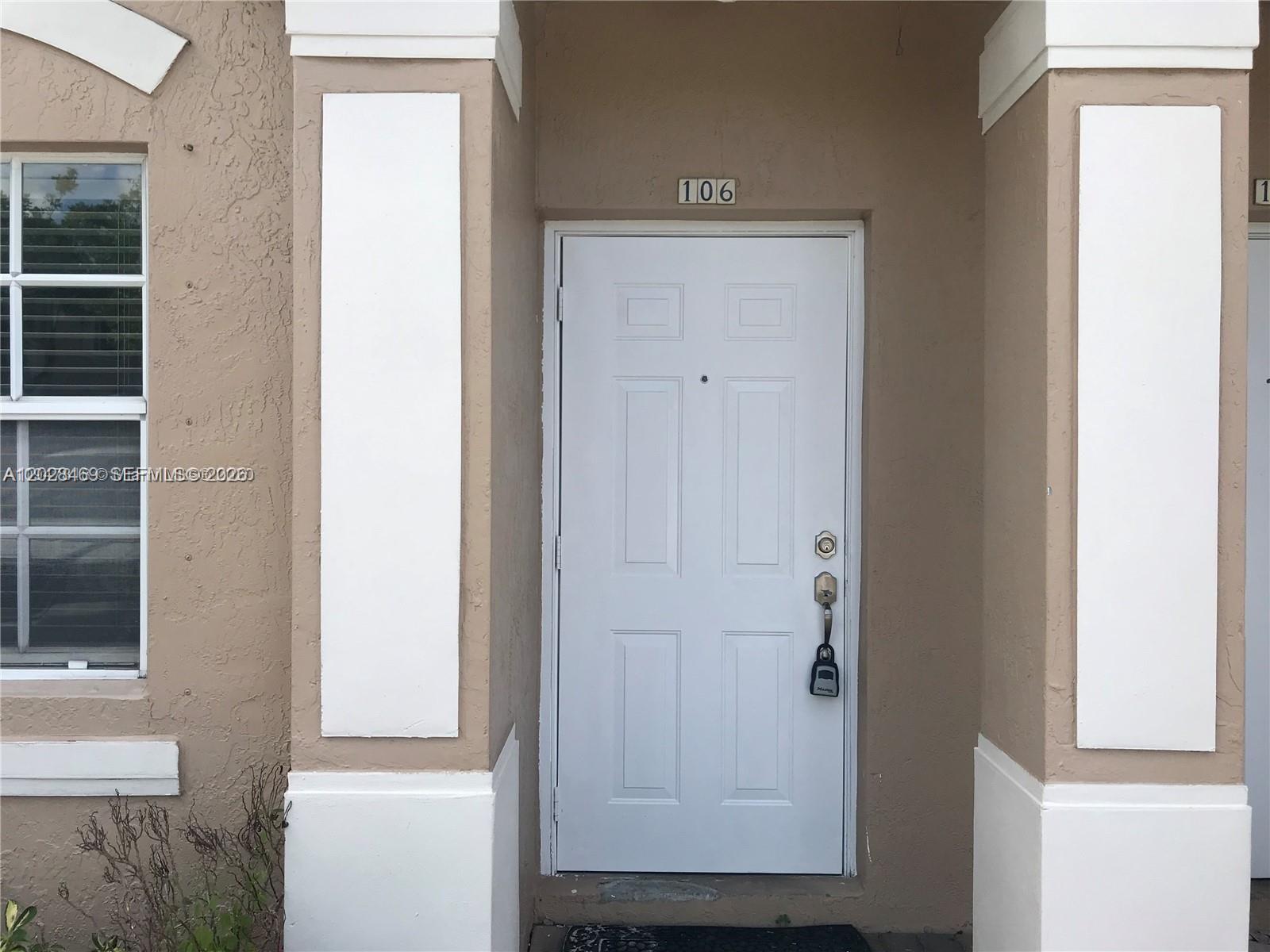 A white front door with a lockbox is set within a tan stucco exterior — 5743 NW 114th Path # 106, Doral FL 33178, DORAL, FL