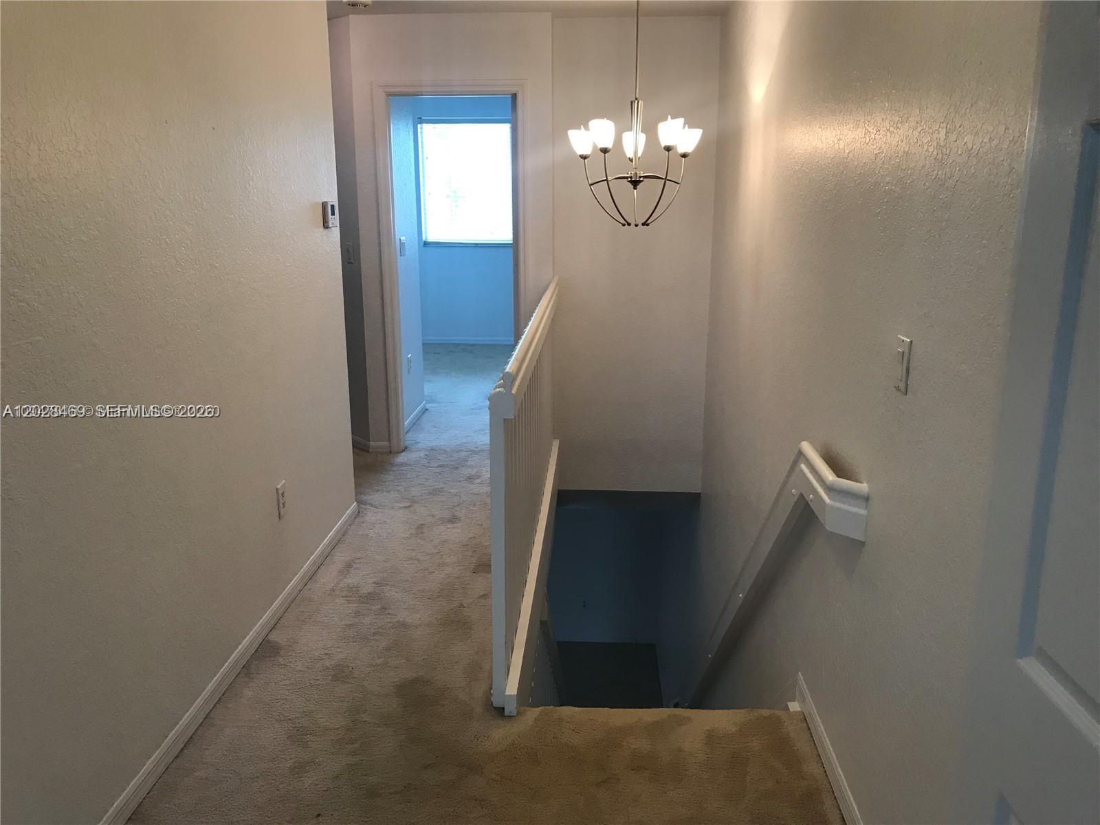 A carpeted hallway features a staircase with a white railing and a hanging chandelier — 5743 NW 114th Path # 106, Doral FL 33178, DORAL, FL