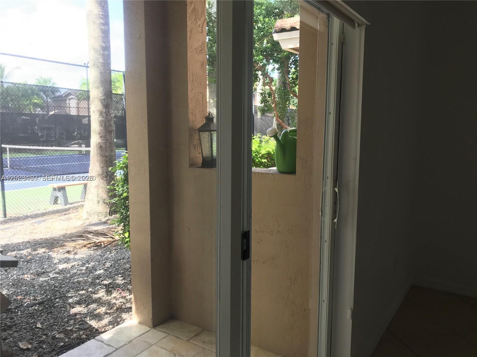 A view from inside looking out through a sliding glass door toward a tennis court — 5743 NW 114th Path # 106, Doral FL 33178, DORAL, FL