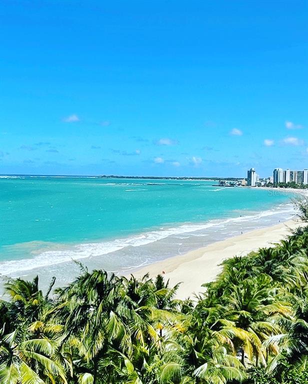 A high-angle view shows a sandy beach, turquoise ocean, and distant coastal buildings — Plaza Atlantico AVE ISLA VERDE UNIT 1002, CAROLINA, PR