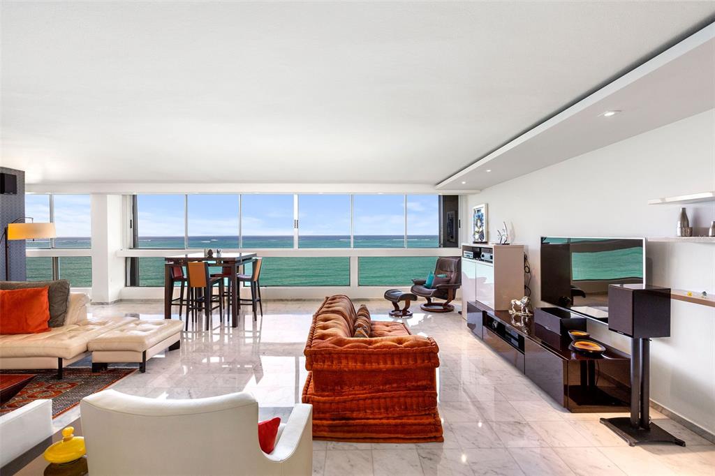 A bright living room with marble floors, a tufted orange sofa, and ocean views — Plaza Atlantico AVE ISLA VERDE UNIT 1002, CAROLINA, PR