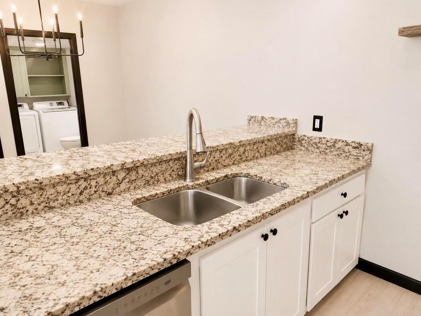 A kitchen sink with a stainless steel faucet set in a granite countertop with white cabinets — 1303 13th Way, West Palm Beach FL 33407, WEST PALM BEACH, FL