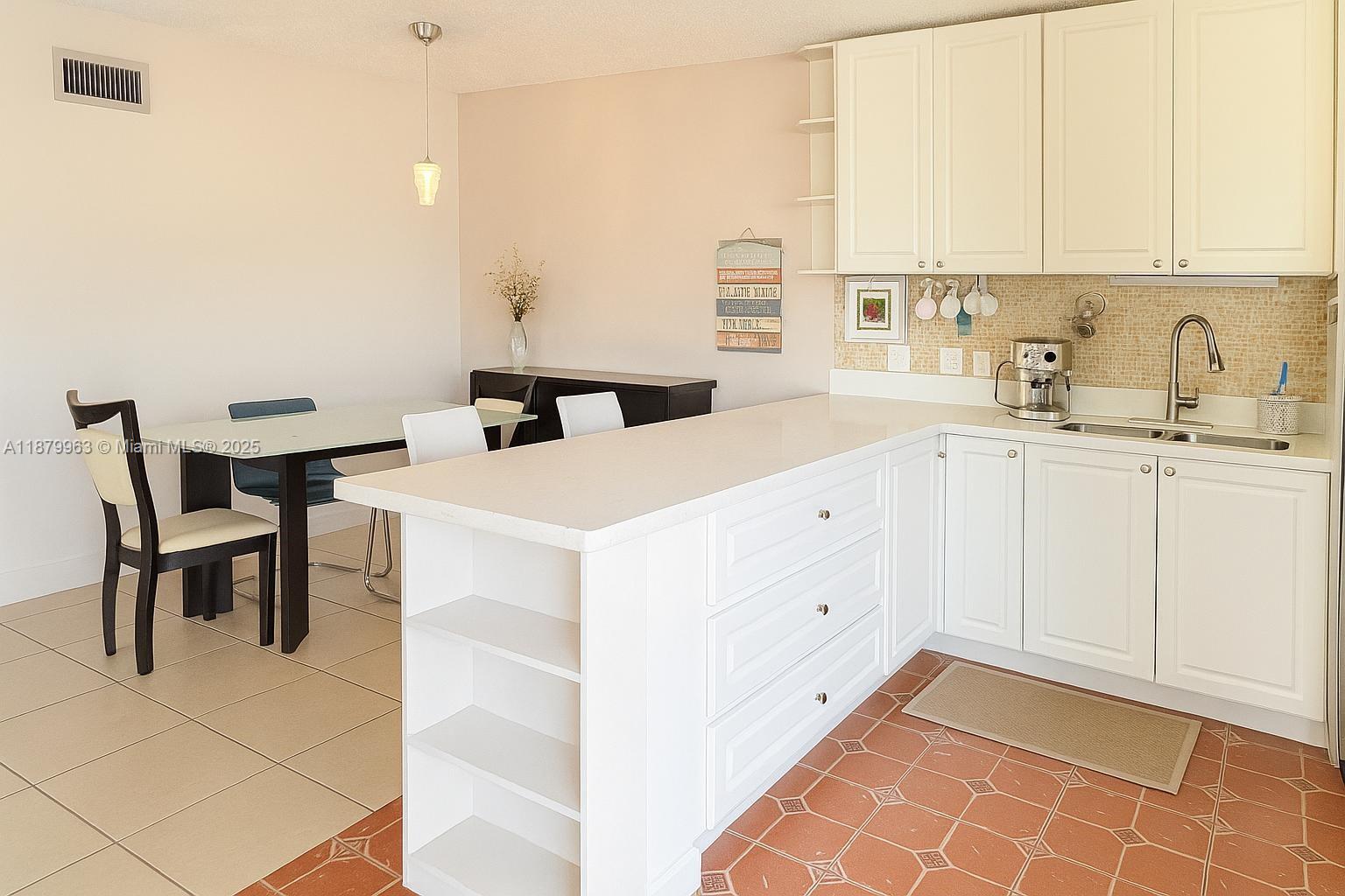 A kitchen features white cabinetry, a central island, and a dining area with tiled flooring — 13781 SW 66th St # 221B, Miami FL 33183, MIAMI, FL