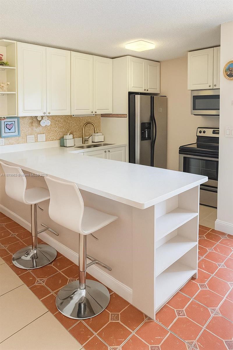 A kitchen features white cabinetry, a breakfast bar with two stools, and terracotta tile flooring — 13781 SW 66th St # 221B, Miami FL 33183, MIAMI, FL