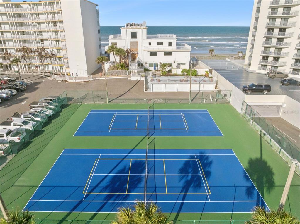 An aerial view shows two blue tennis courts located between two large beachside apartment buildings — 5203 S ATLANTIC AVENUE UNIT 314B, NEW SMYRNA BEACH, FL