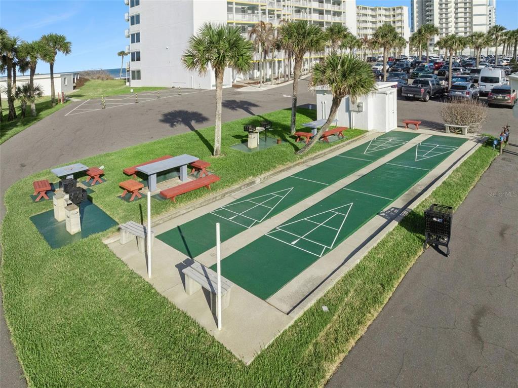 An outdoor recreation area features two shuffleboard courts, picnic tables, and grills near a building — 5203 S ATLANTIC AVENUE UNIT 314B, NEW SMYRNA BEACH, FL
