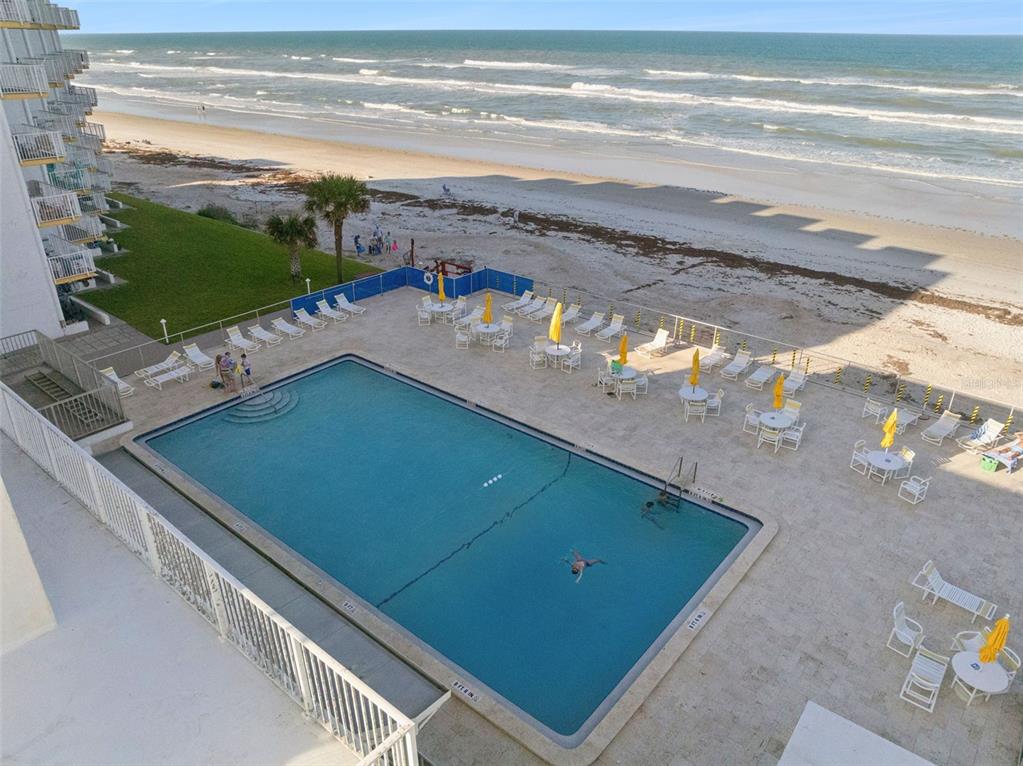 An elevated view shows a rectangular swimming pool on a patio beside a sandy beach — 5203 S ATLANTIC AVENUE UNIT 314B, NEW SMYRNA BEACH, FL