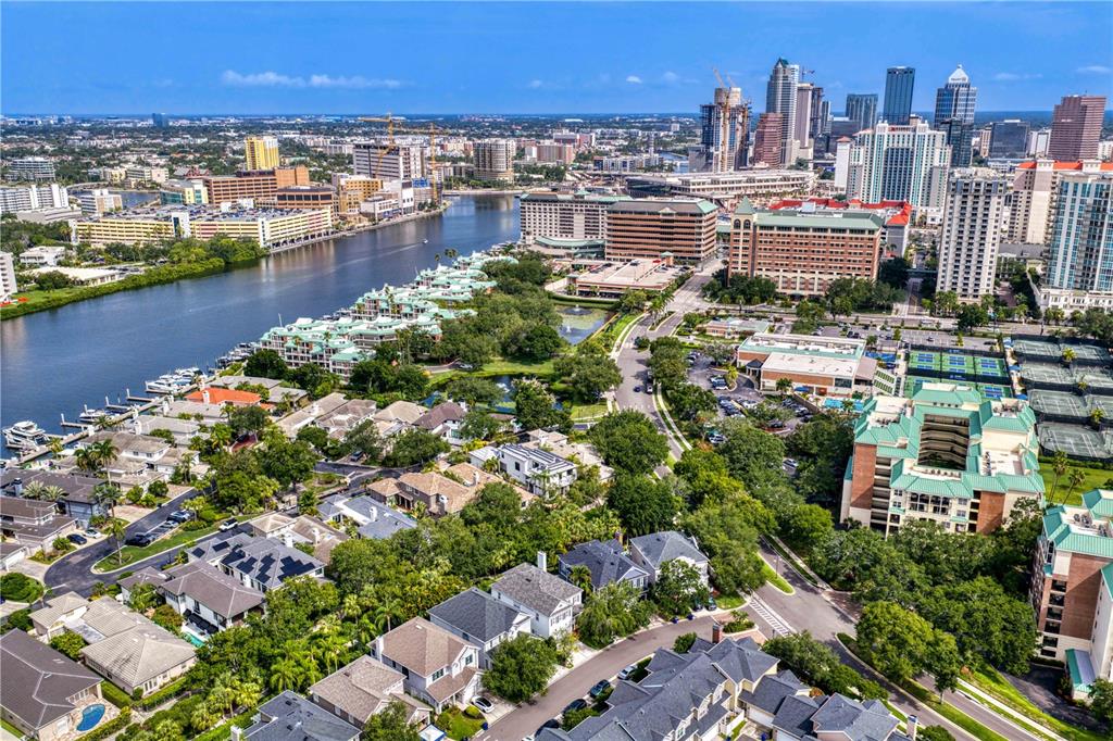 An aerial view shows a residential neighborhood along a river with a city skyline nearby — 905 HARBOUR BAY DRIVE, TAMPA, FL