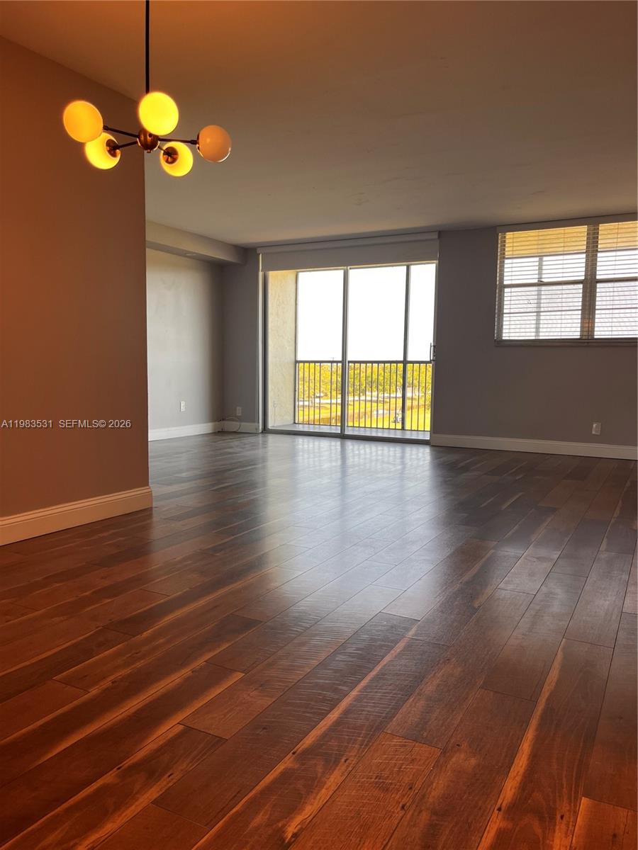 An empty living room features dark wood flooring, a modern chandelier, and a sliding glass door — 3100 W Rolling Hills Cir # 403, Davie FL 33328, DAVIE, FL