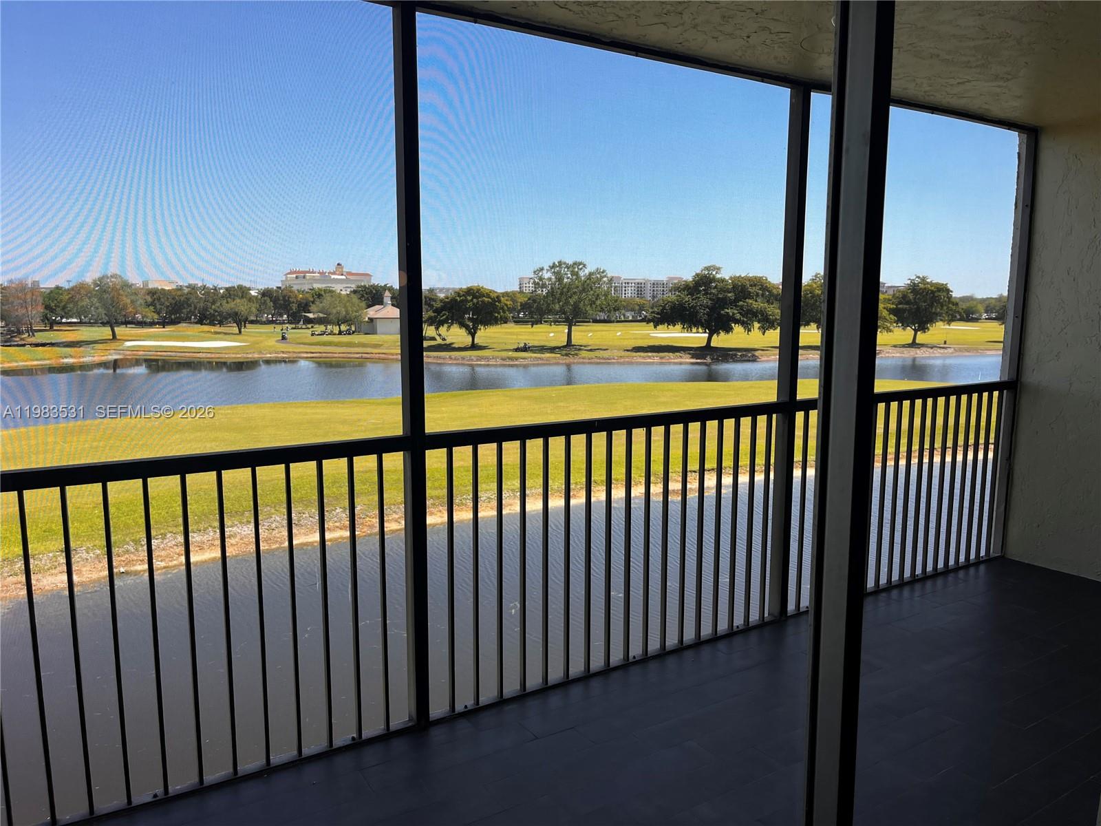 A screened-in balcony overlooks a lake and a golf course under a clear sky — 3100 W Rolling Hills Cir # 403, Davie FL 33328, DAVIE, FL