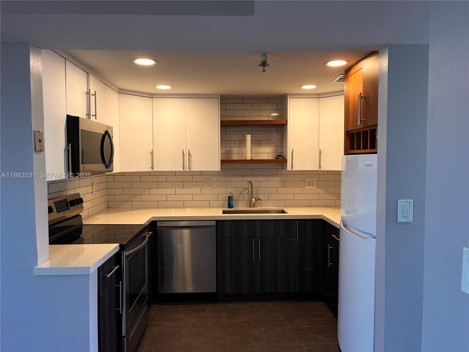A kitchen features white upper cabinets, dark lower cabinets, stainless steel appliances, and subway tile — 3100 W Rolling Hills Cir # 403, Davie FL 33328, DAVIE, FL