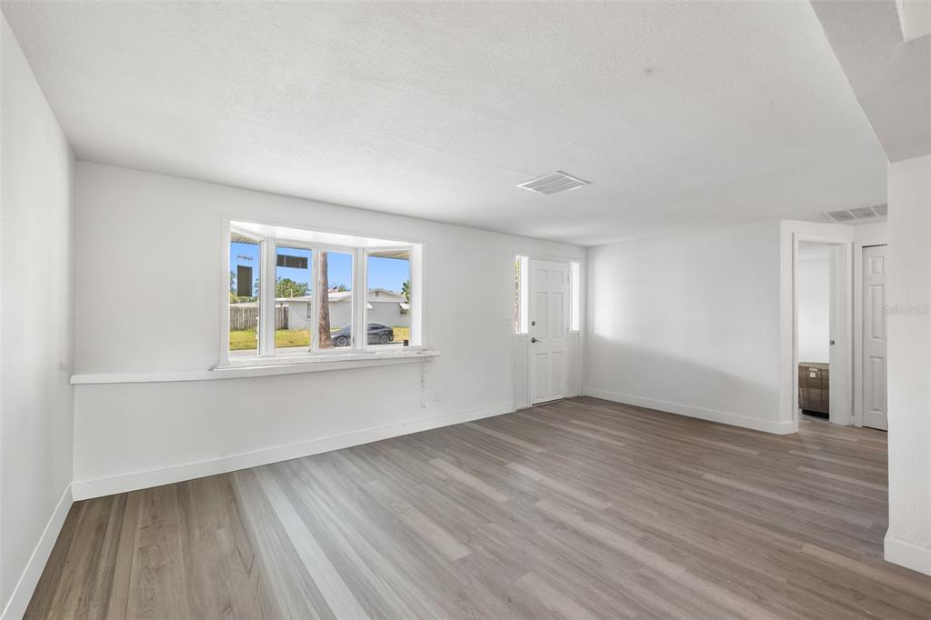 A bright living room features white walls, wood-look flooring, a bay window, and a door — 4711 BEACON HILL DRIVE, NEW PORT RICHEY, FL