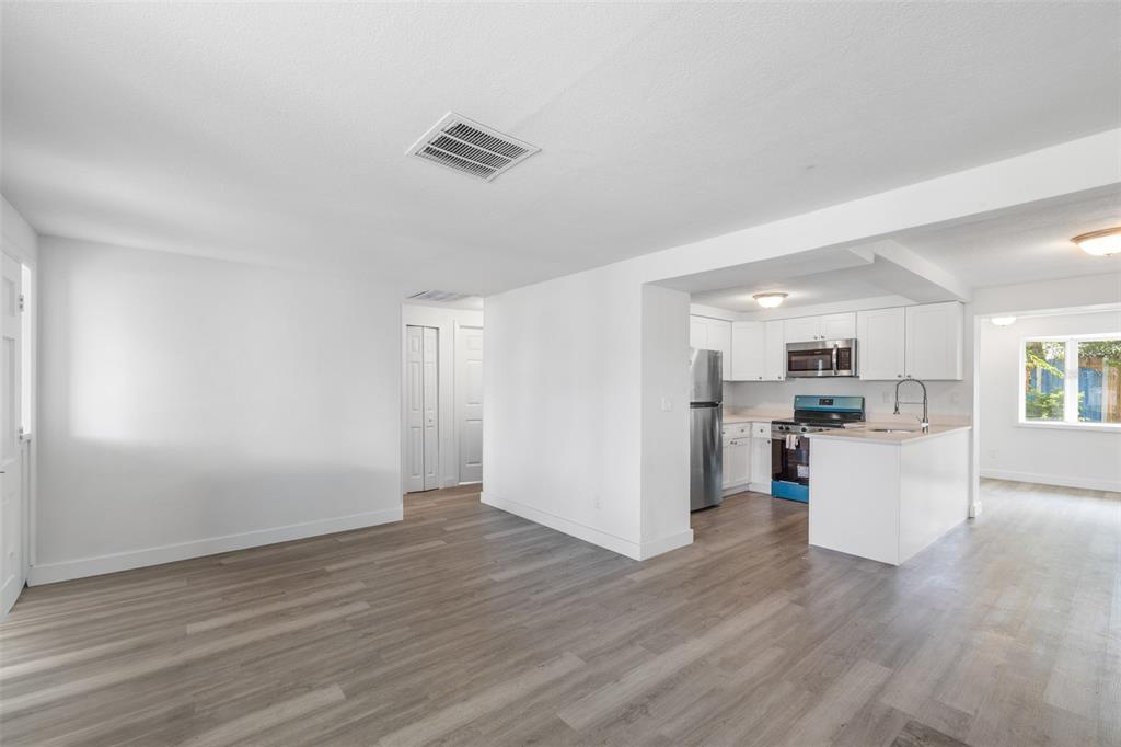 An open-concept living area features light wood-look flooring and a kitchen with white cabinetry — 4711 BEACON HILL DRIVE, NEW PORT RICHEY, FL