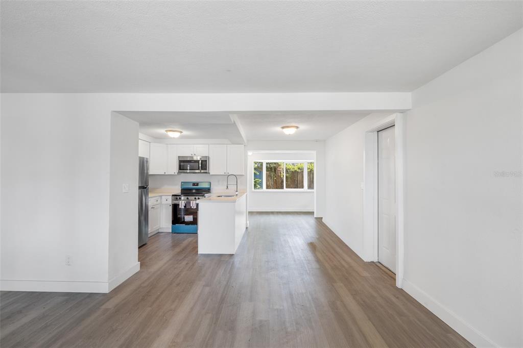 A bright, open-concept kitchen and living area featuring white cabinetry, stainless appliances, and wood-look flooring — 4711 BEACON HILL DRIVE, NEW PORT RICHEY, FL
