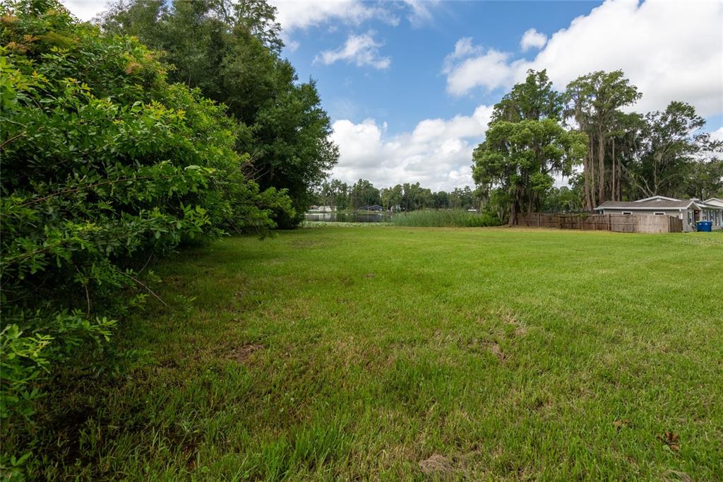 A grassy vacant lot features mature trees and a view of a distant lake — 21414 LAKE SHARON DRIVE, LAND O LAKES, FL