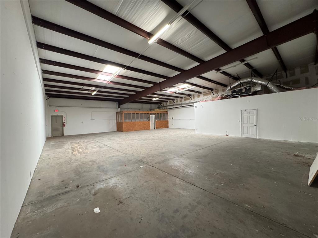 An open industrial warehouse space features a concrete floor, exposed ceiling beams, and a partition — 1408 HAMLIN AVENUE, ST CLOUD, FL