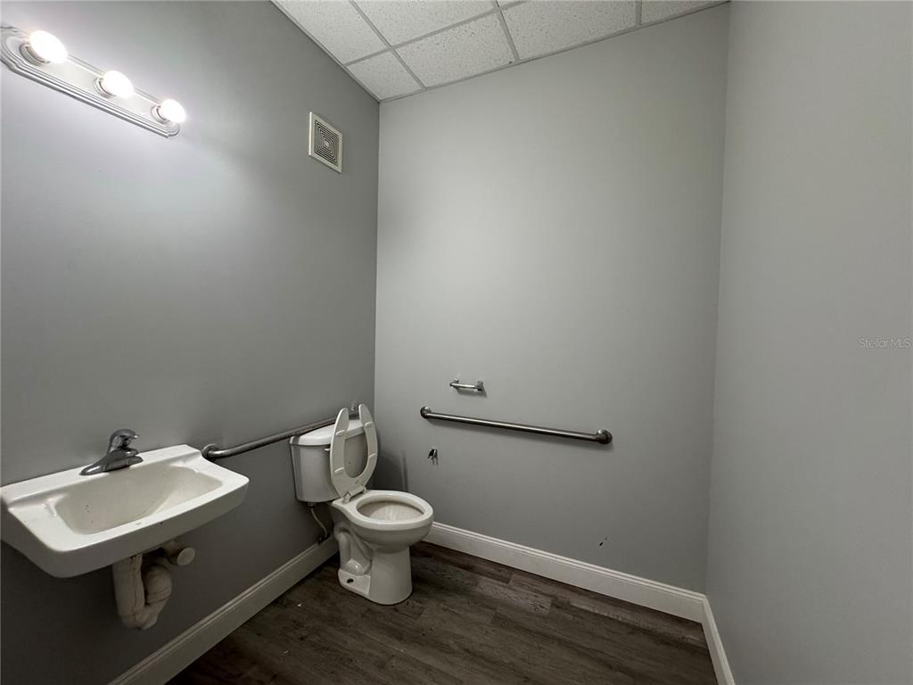 A small, gray-walled restroom features a wall-mounted sink, a toilet, and a grab bar — 1408 HAMLIN AVENUE, ST CLOUD, FL