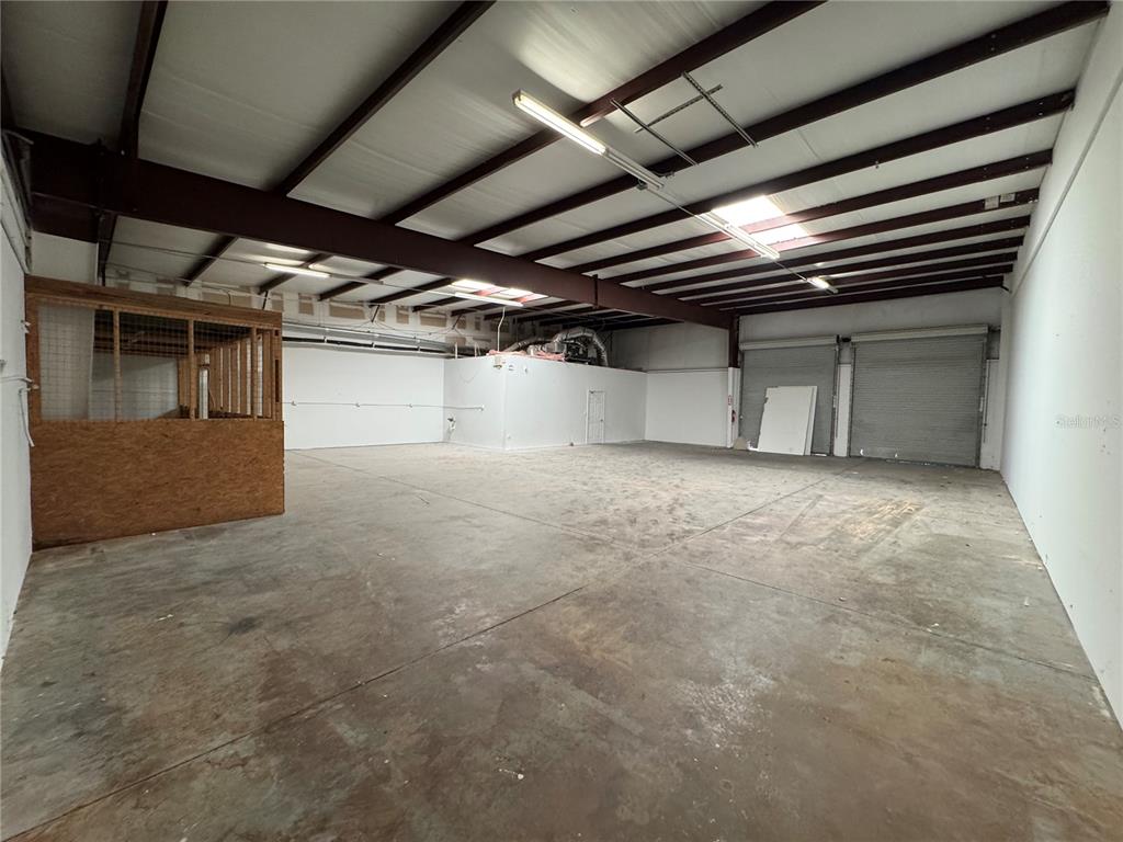 An empty warehouse space features a concrete floor, metal roll-up doors, and a wooden stall — 1408 HAMLIN AVENUE, ST CLOUD, FL