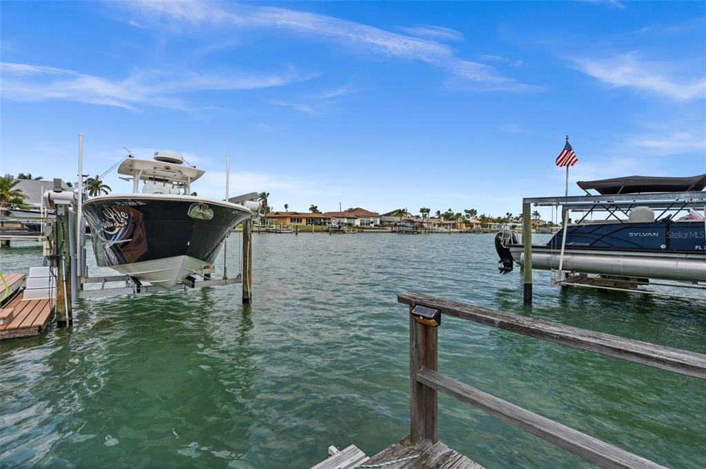 Two boats are docked on lifts in a canal with houses in the background — 710 116TH AVENUE, TREASURE ISLAND, FL