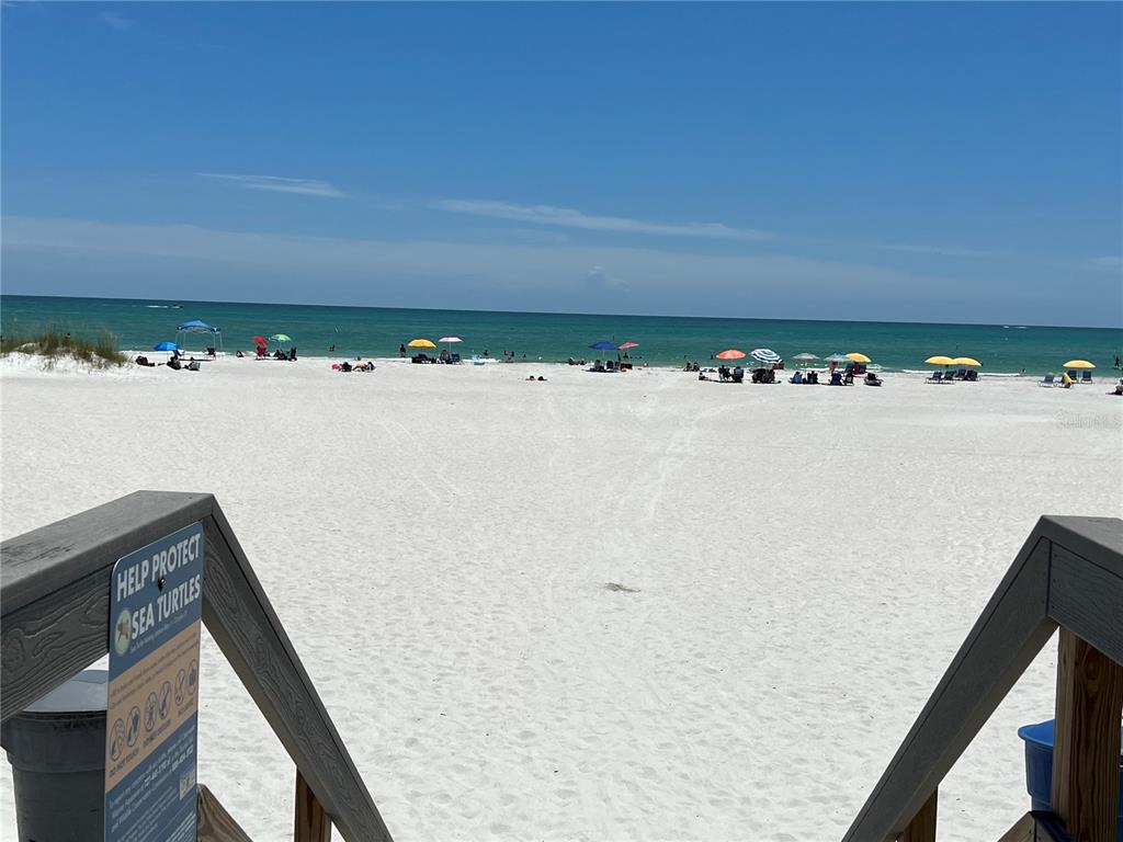 A wooden staircase leads down to a white sand beach with many colorful umbrellas — 710 116TH AVENUE, TREASURE ISLAND, FL