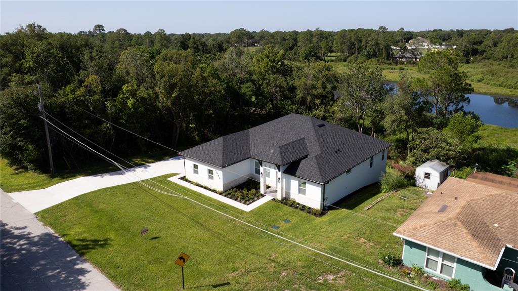 An aerial view shows a white house with a dark roof next to a pond — 1989 MONTEREY DRIVE, DELTONA, FL