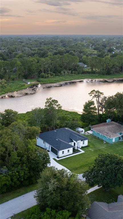An aerial view shows a white house with a dark roof near a river — 1989 MONTEREY DRIVE, DELTONA, FL