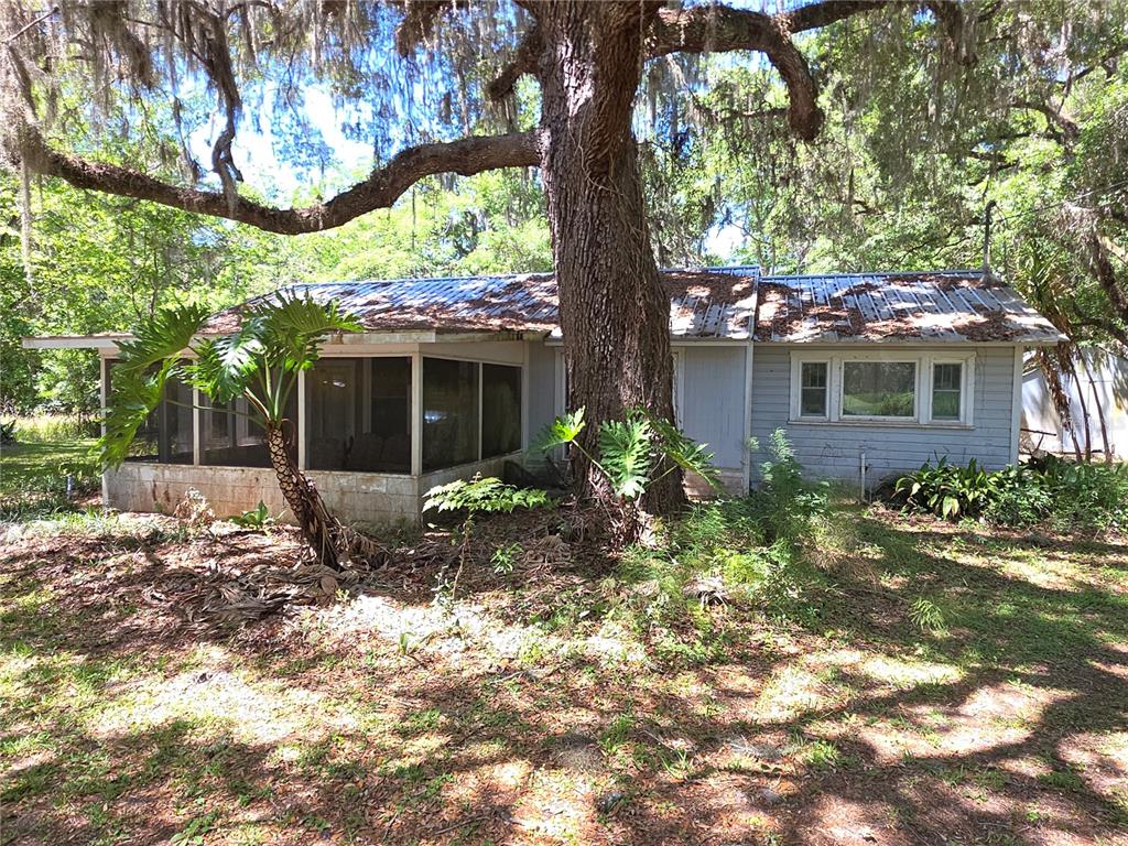 A single-story house with a screened porch and metal roof sits beneath a large tree — 13499 OLD CRYSTAL RIVER ROAD, BROOKSVILLE, FL