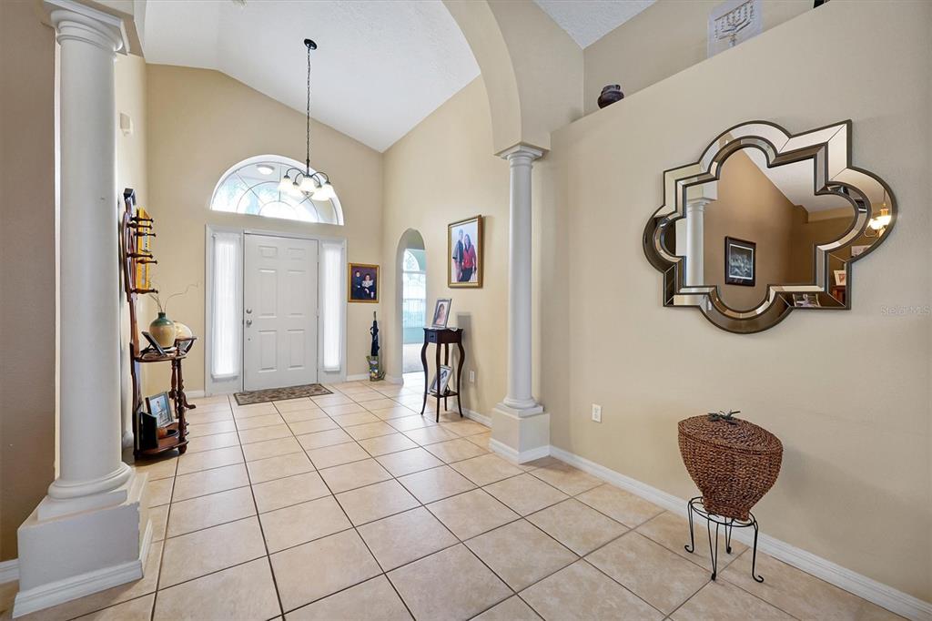 A tiled foyer features a high ceiling, white columns, a decorative mirror, and a front door — 816 KNIGHTSBRIDGE CIRCLE, DAVENPORT, FL