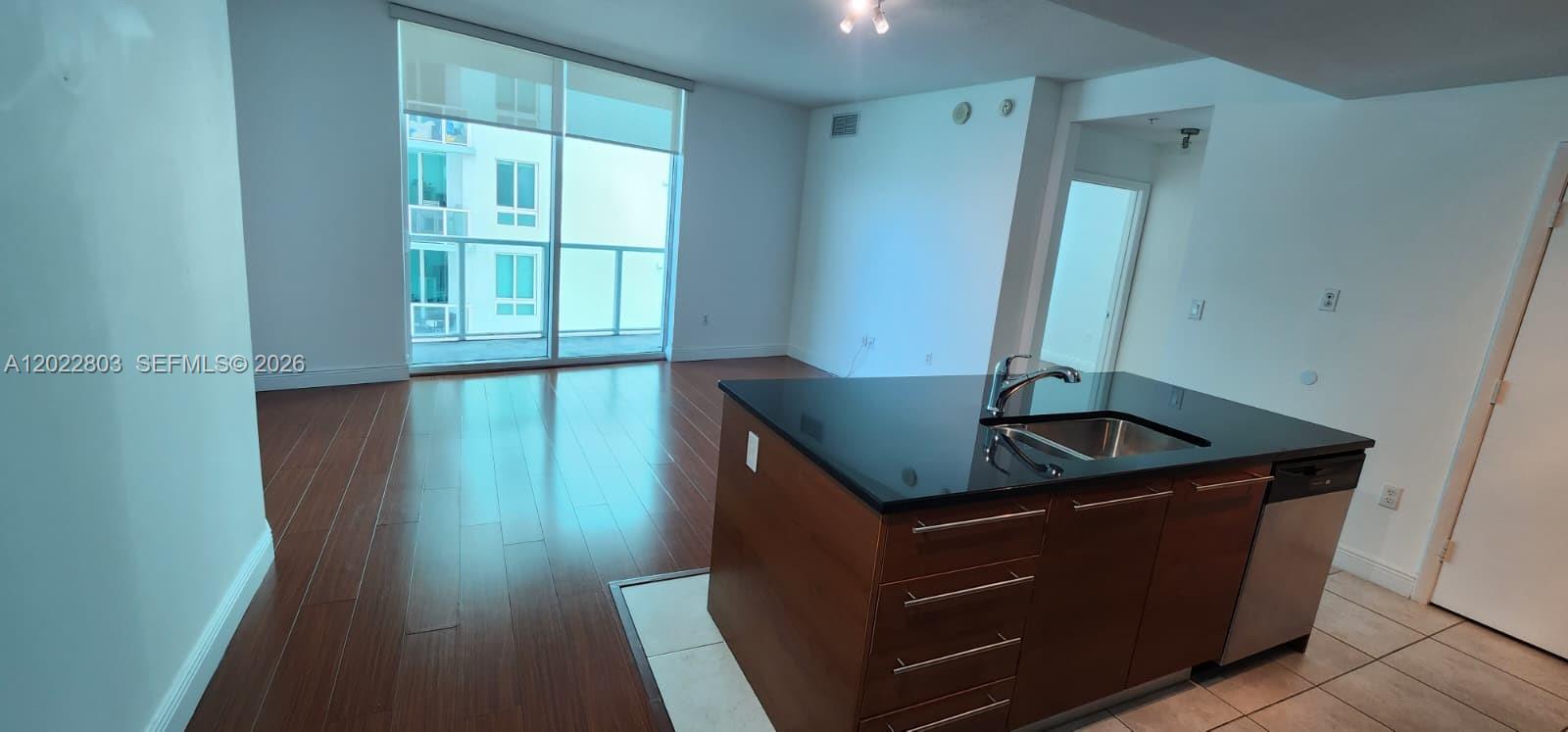 A kitchen island with a black countertop and wood cabinets sits in an open-plan room — 1900 N Bayshore Dr # 3717, Miami FL 33132, MIAMI, FL