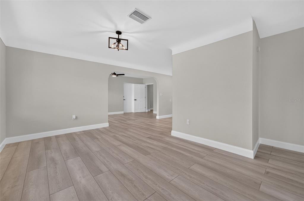An interior view shows a room with light wood-look flooring, gray walls, and arched doorways — 763 65TH AVENUE S, ST PETERSBURG, FL