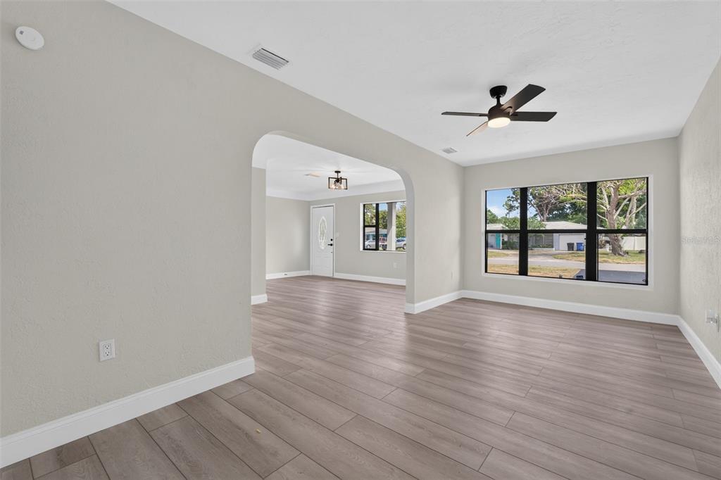 An interior view of a living room with light wood-look flooring and an arched entryway — 763 65TH AVENUE S, ST PETERSBURG, FL