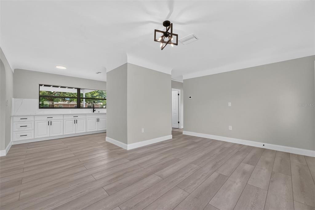 A bright, open-concept room features light gray walls, wood-look flooring, and a white kitchen area — 763 65TH AVENUE S, ST PETERSBURG, FL