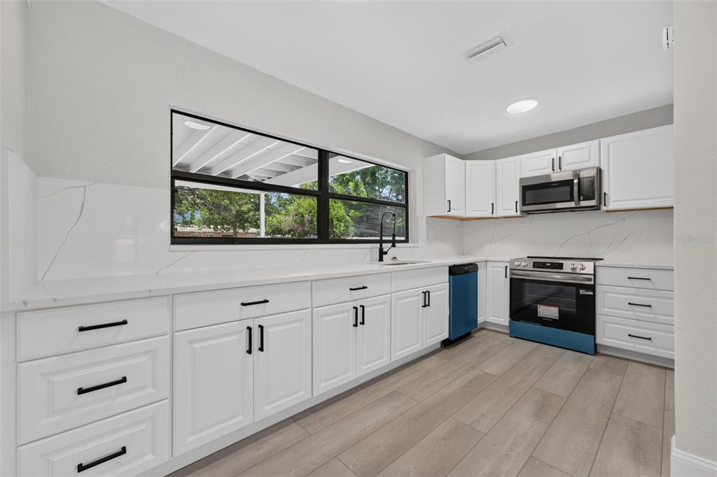 A kitchen features white cabinets, marble-look countertops, stainless steel appliances, and light wood-look flooring — 763 65TH AVENUE S, ST PETERSBURG, FL