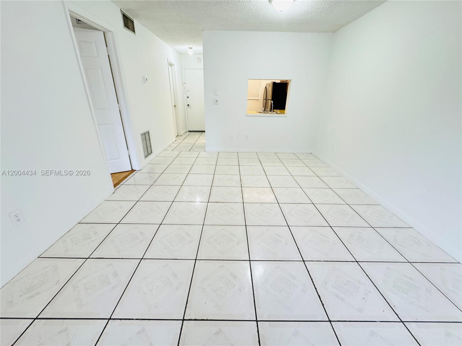 An empty room with white tiled floors, white walls, and a small kitchen pass-through window — 2800 NW 56th Ave # D102, Lauderhill FL 33313, LAUDERHILL, FL