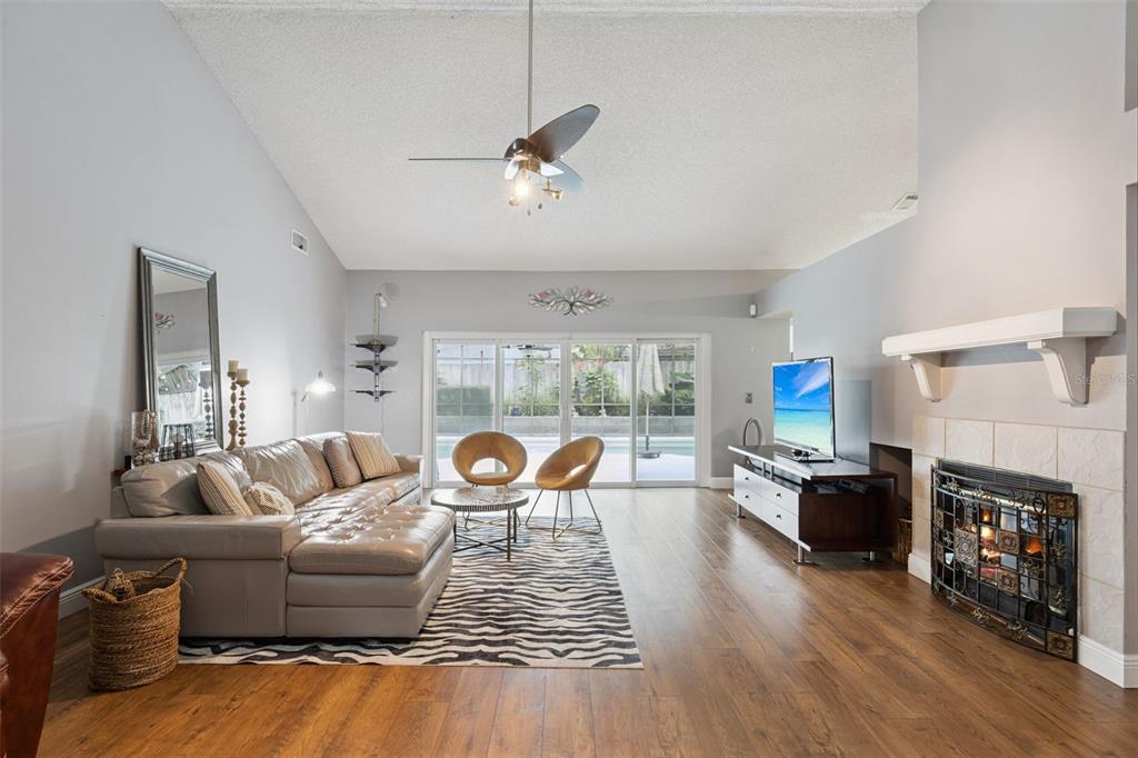 A living room features a vaulted ceiling, wood-look flooring, a fireplace, and sliding glass doors — 680 TOMLINSON TERRACE, LAKE MARY, FL