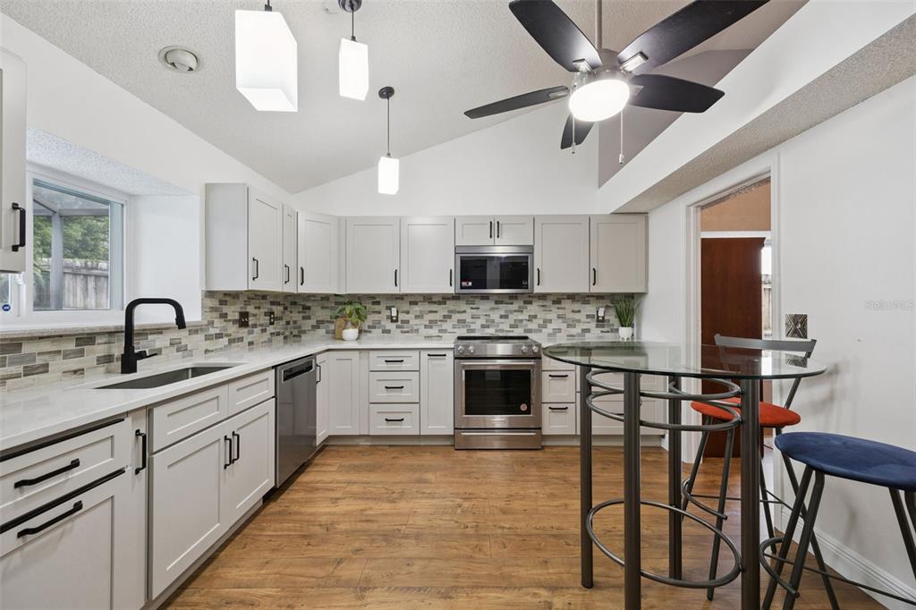 A kitchen features light gray cabinets, stainless steel appliances, a tile backsplash, and wood-look flooring — 680 TOMLINSON TERRACE, LAKE MARY, FL